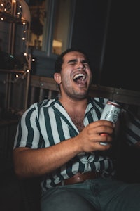 a man laughing while holding a beer can