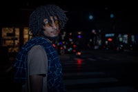 a man with dreadlocks standing on a street at night