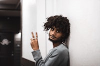 a man with dreadlocks leaning against a wall