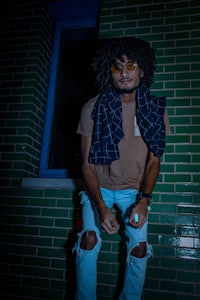 a man with dreadlocks sitting on a brick wall